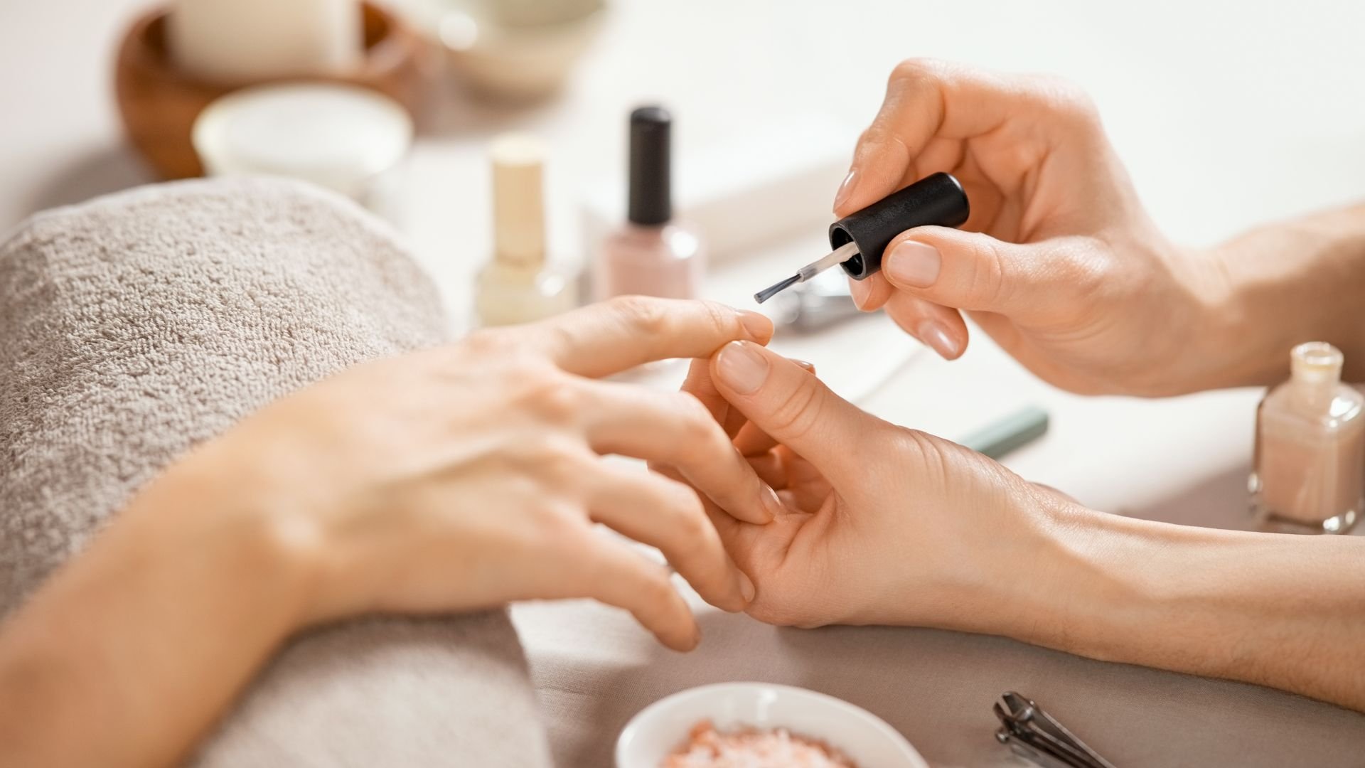 Hands applying nail polish during a manicure with beauty products nearby