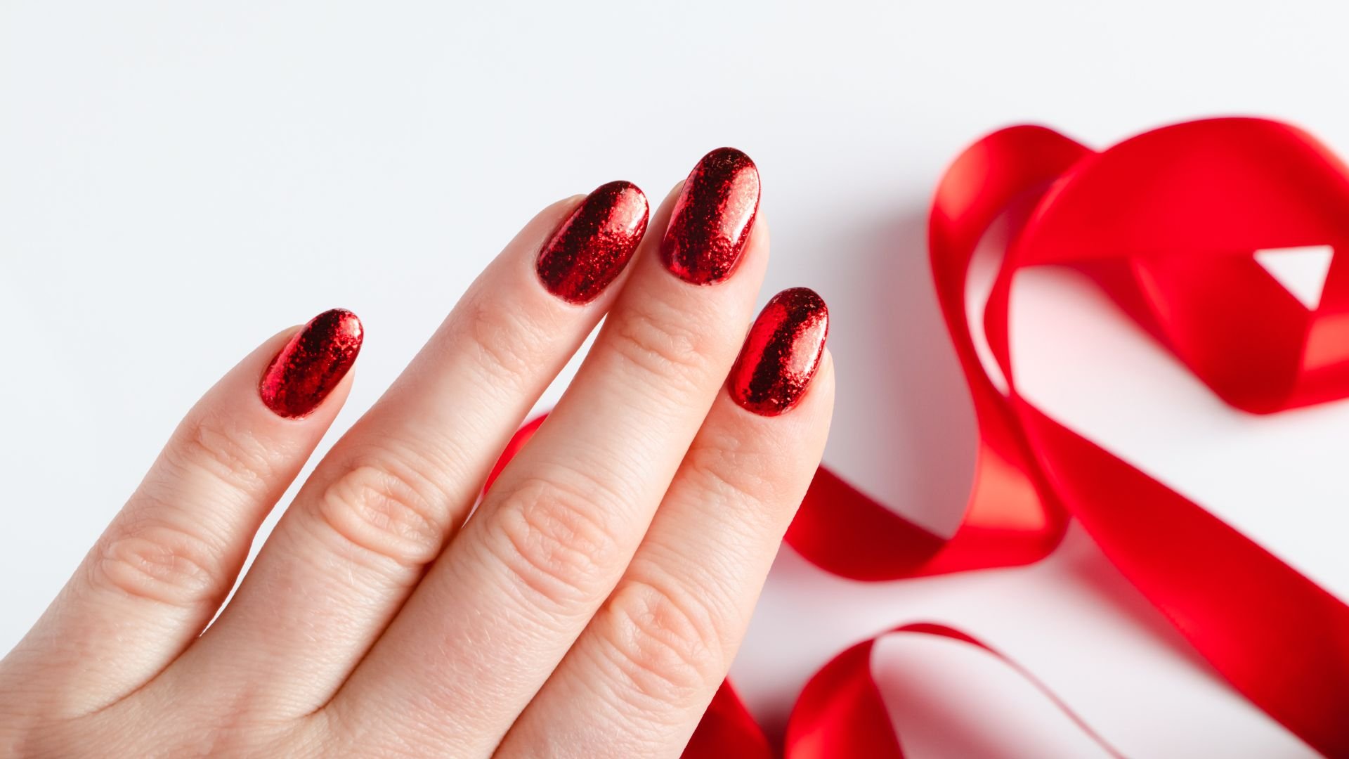 Sparkly red metallic nail polish with red ribbon in background