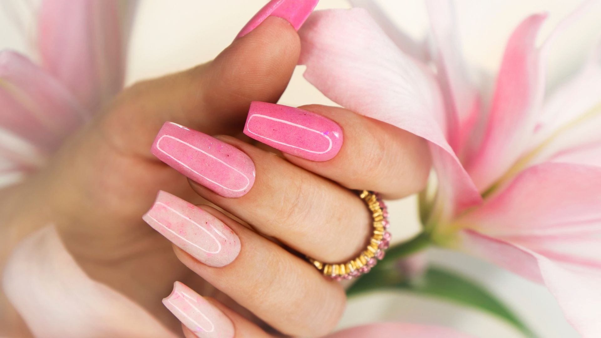 Pink ombré manicure with gold ring against soft pink flower background