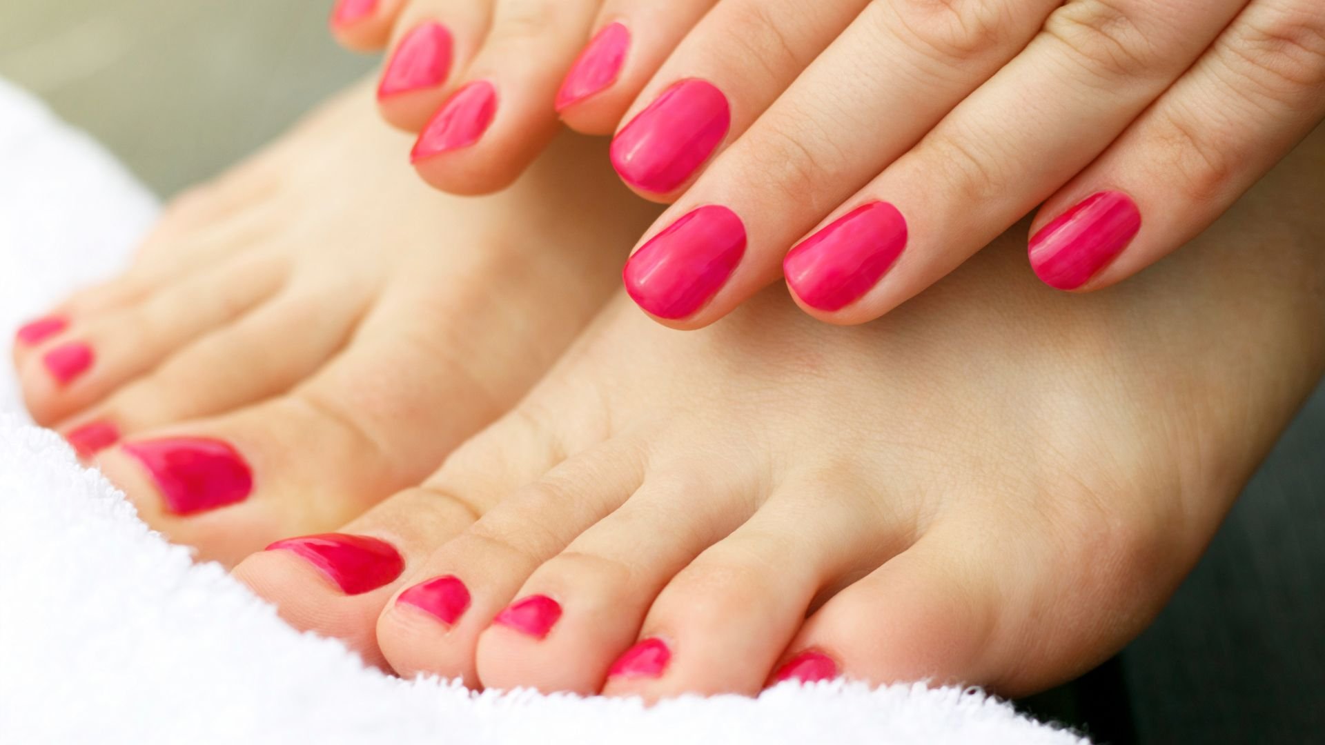 Hands and feet with bright pink manicure and pedicure on white towel