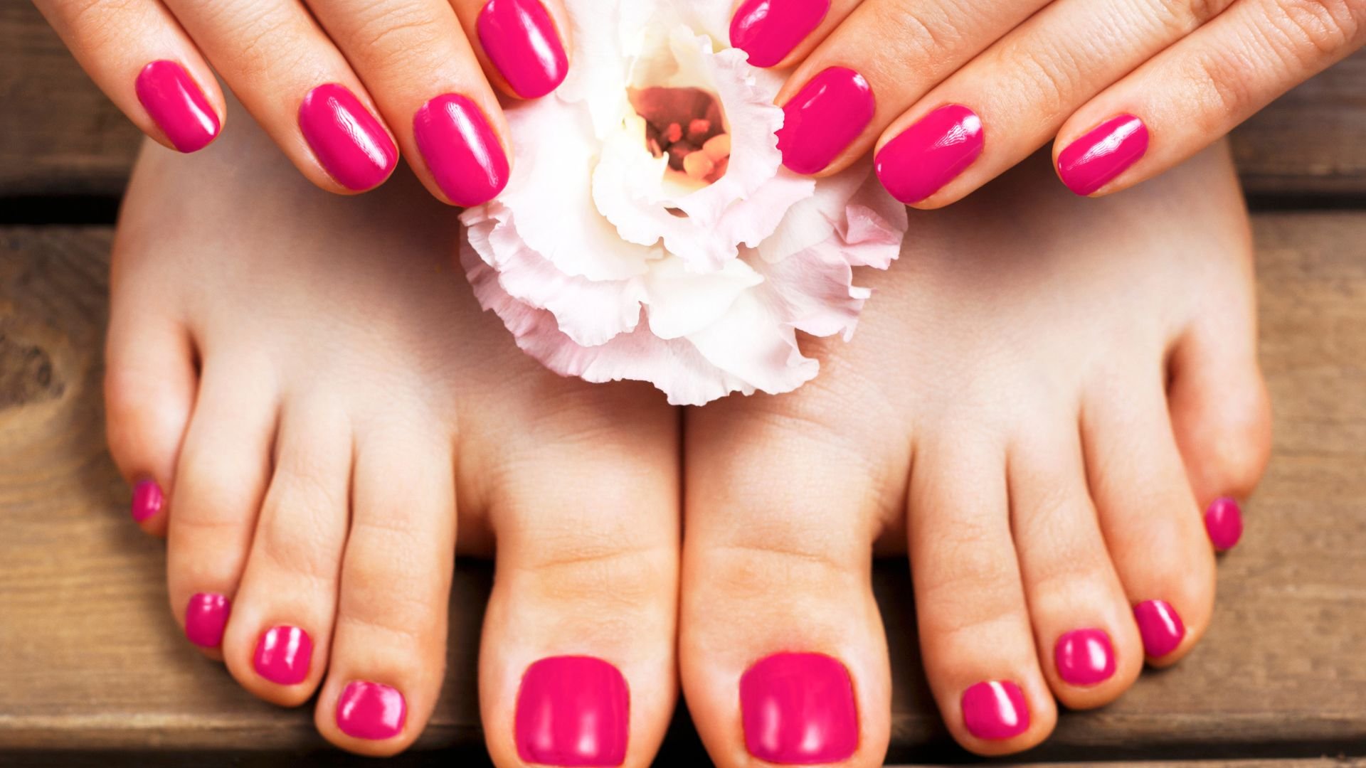 Pink nail polish pedicure with white flower on wooden surface