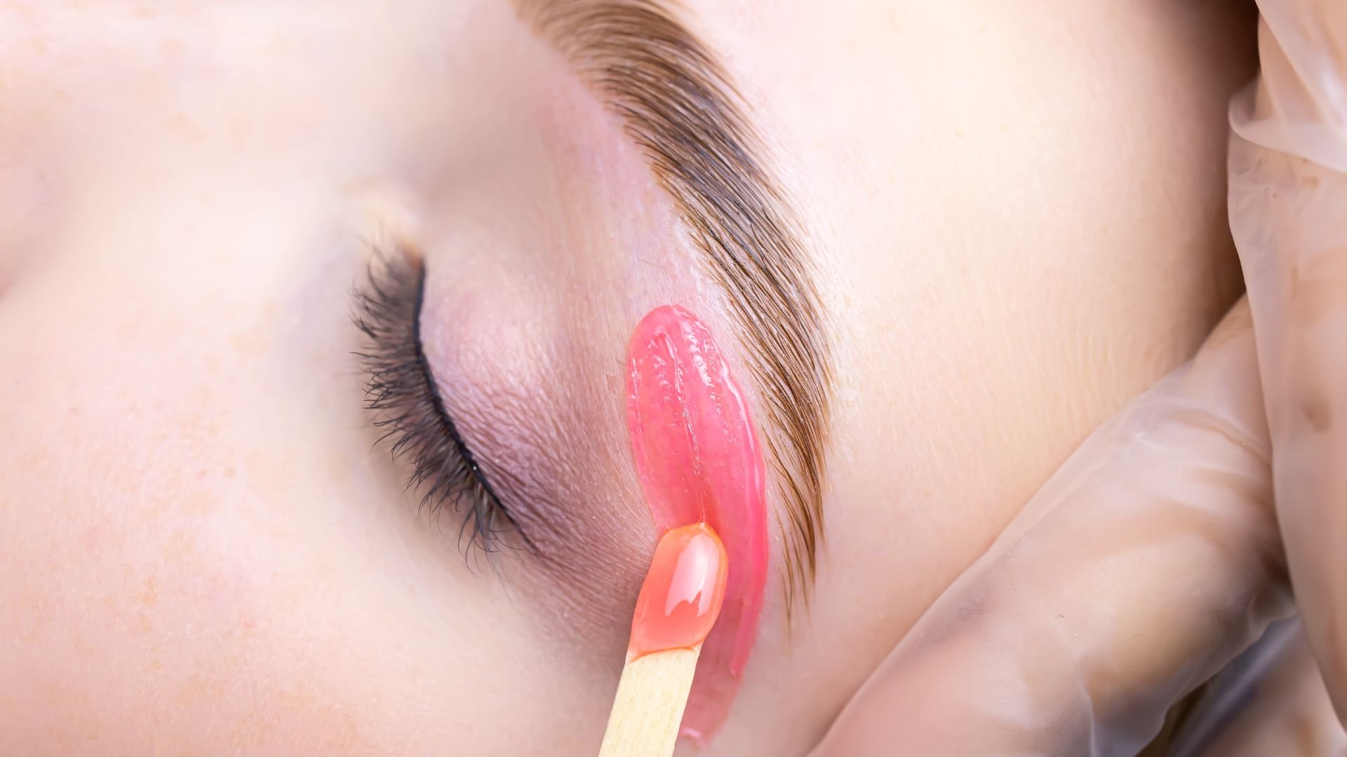 Close-up of pink lip gloss being applied to closed eyelid