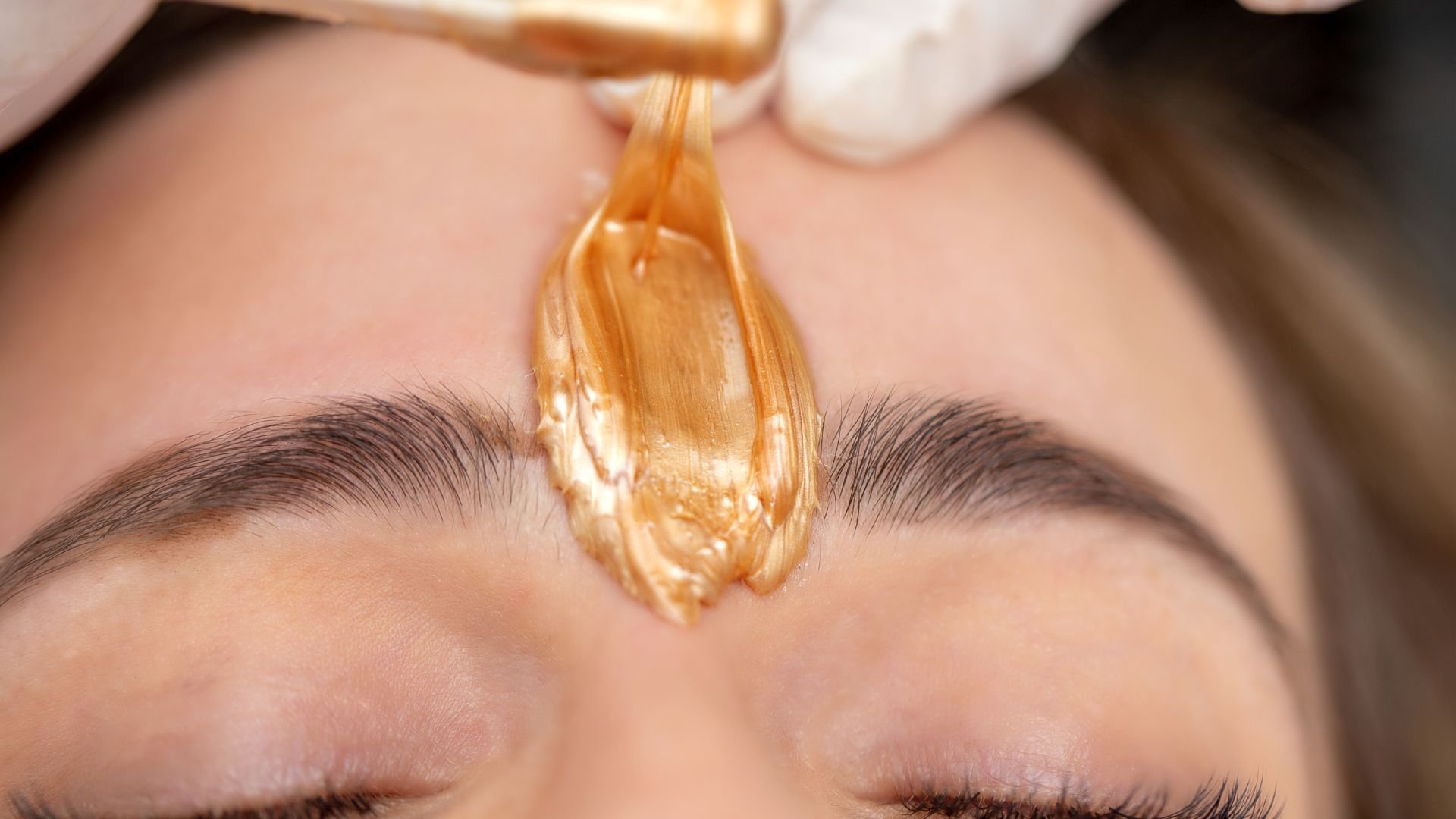 Close-up of eyebrow hair removal using golden-colored sugar wax
