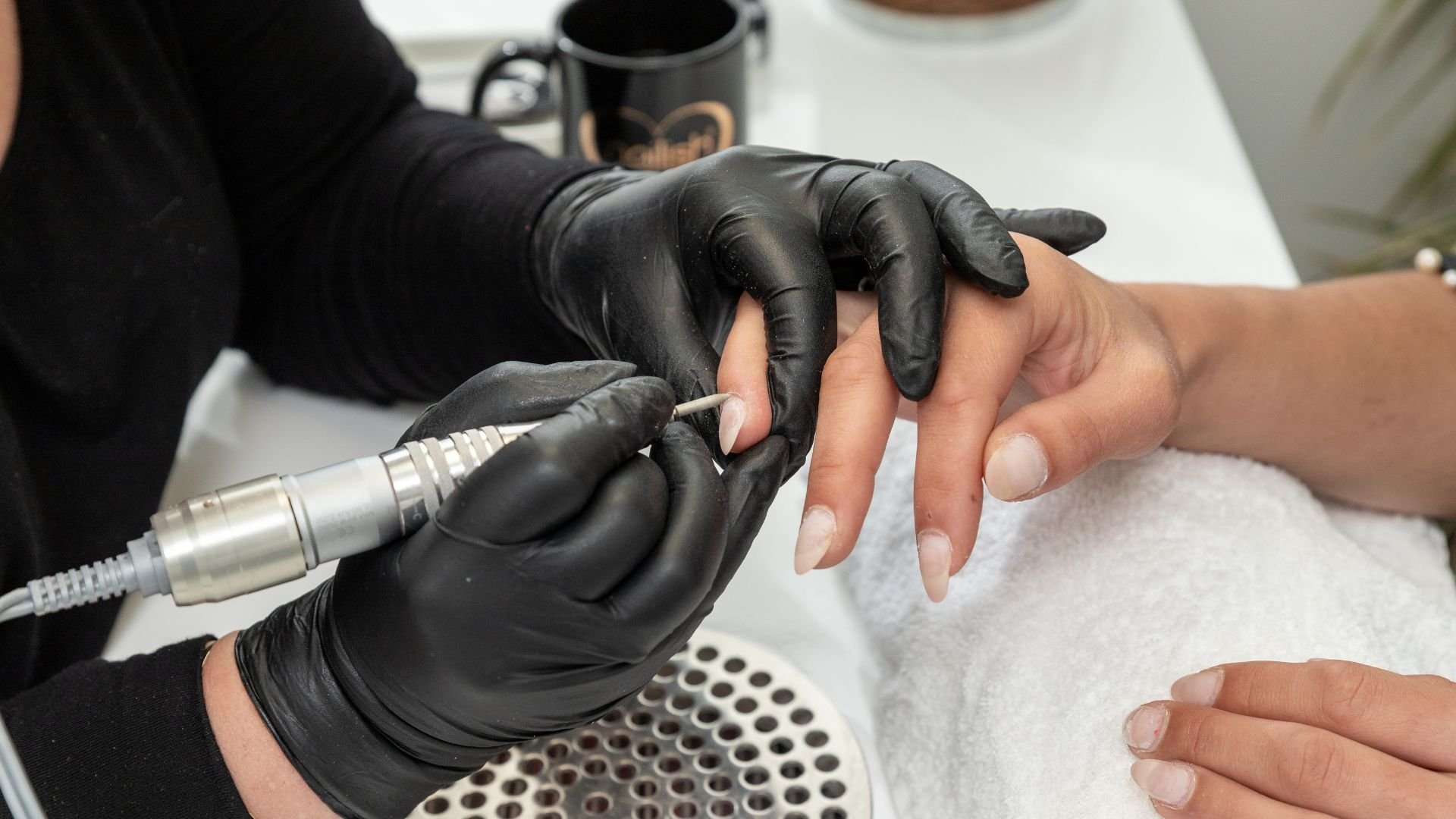 Nail technician in black gloves using electric drill for manicure